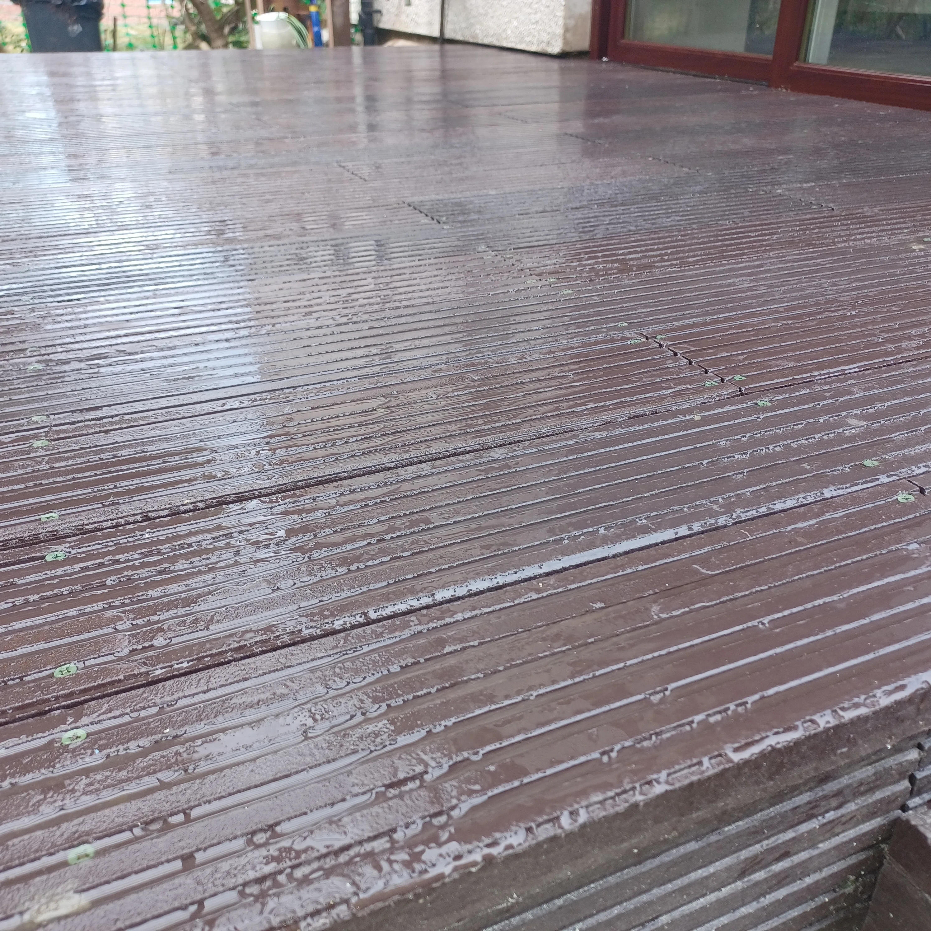Installed brown recycled plastic decking boards in rain — grooved profile visible